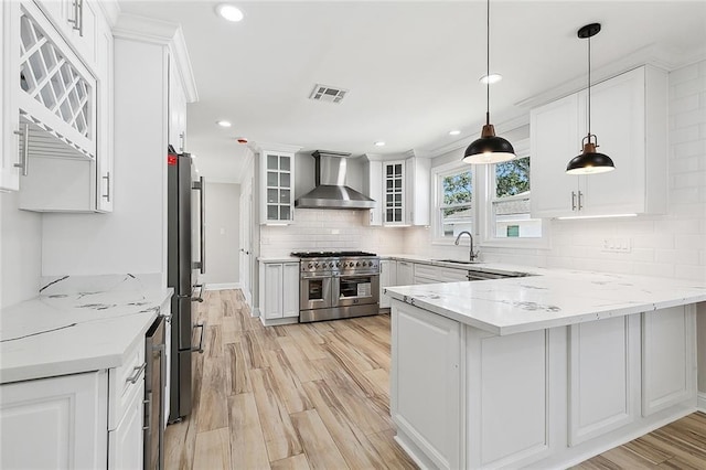 kitchen with wall chimney range hood, hanging light fixtures, white cabinets, and appliances with stainless steel finishes