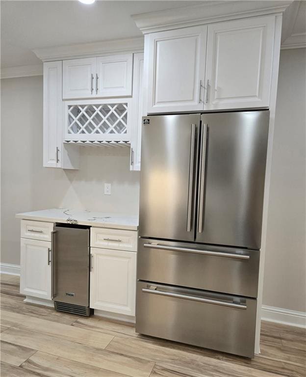 kitchen with ornamental molding, white cabinets, stainless steel refrigerator, and light hardwood / wood-style flooring