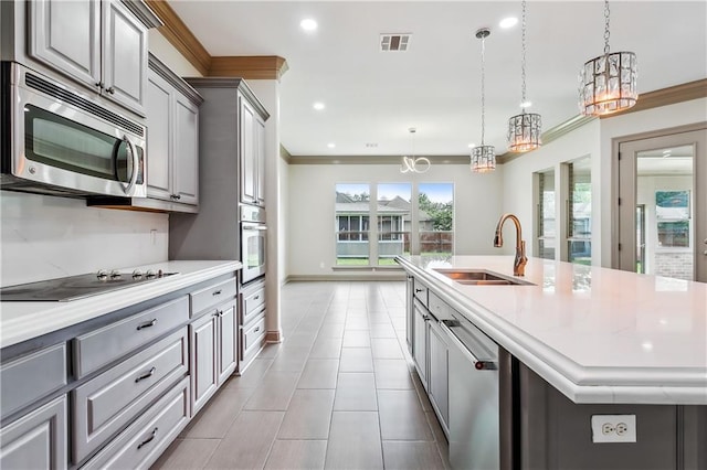 kitchen with appliances with stainless steel finishes, gray cabinets, hanging light fixtures, and a center island with sink