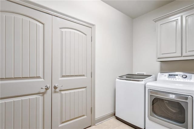 clothes washing area with washer and dryer, light tile patterned floors, and cabinets