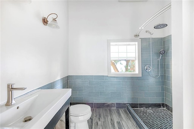 bathroom with tiled shower, toilet, tile walls, and sink