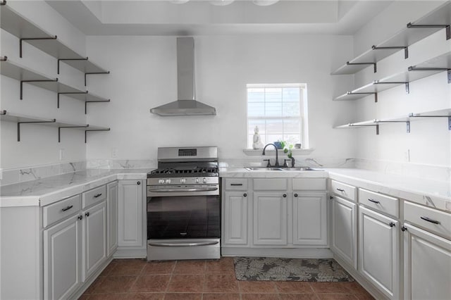 kitchen with dark tile patterned flooring, stainless steel range with gas cooktop, sink, wall chimney exhaust hood, and white cabinetry