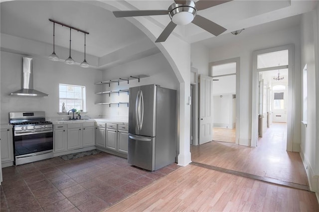 kitchen featuring sink, hanging light fixtures, wall chimney range hood, ceiling fan with notable chandelier, and appliances with stainless steel finishes