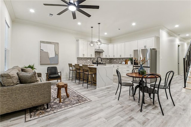 dining room featuring crown molding, ceiling fan, sink, and light wood-type flooring