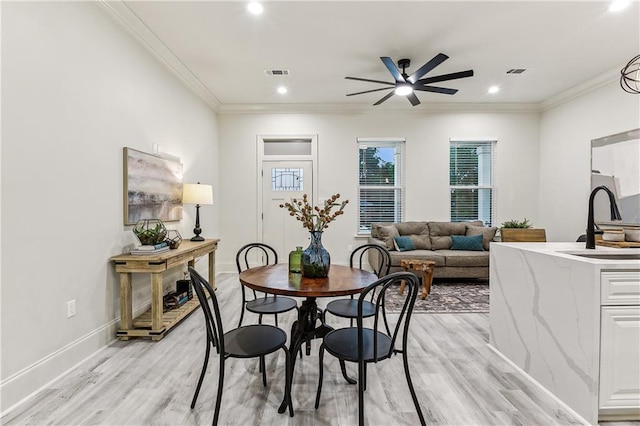 dining area with ornamental molding, sink, and light hardwood / wood-style floors