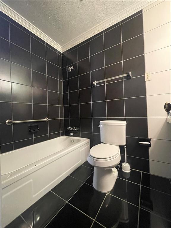 bathroom with tile patterned floors, bathing tub / shower combination, a textured ceiling, toilet, and tile walls