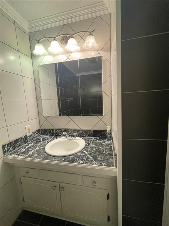 bathroom with decorative backsplash, ornamental molding, vanity, tile walls, and tile patterned flooring