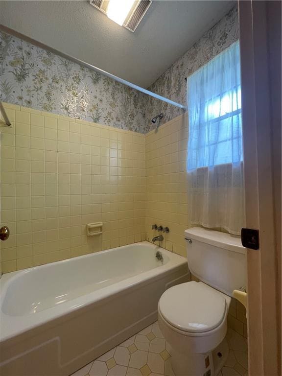 bathroom with tile patterned floors, tiled shower / bath combo, a textured ceiling, and toilet