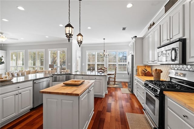 kitchen with kitchen peninsula, stainless steel appliances, pendant lighting, butcher block countertops, and white cabinetry