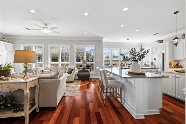 kitchen with white cabinetry, hanging light fixtures, stainless steel fridge with ice dispenser, dark stone countertops, and a kitchen island