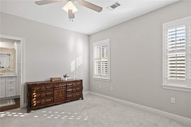 bedroom with multiple windows, ensuite bathroom, ceiling fan, and light carpet