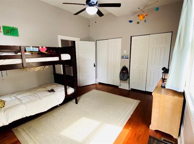 bedroom with dark hardwood / wood-style flooring, two closets, and ceiling fan