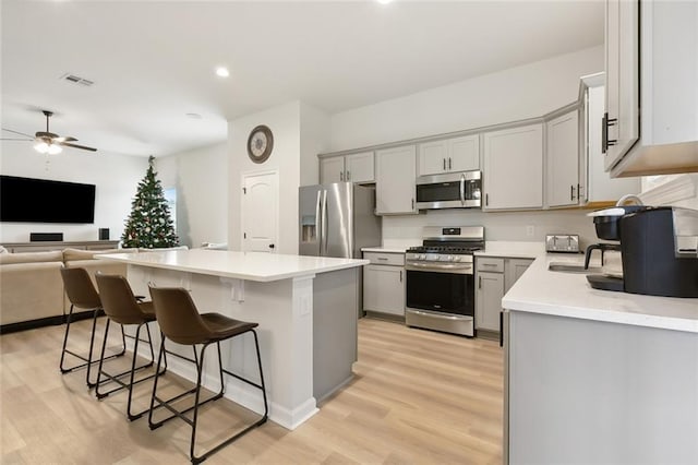 kitchen with gray cabinetry, ceiling fan, a center island, light hardwood / wood-style flooring, and appliances with stainless steel finishes