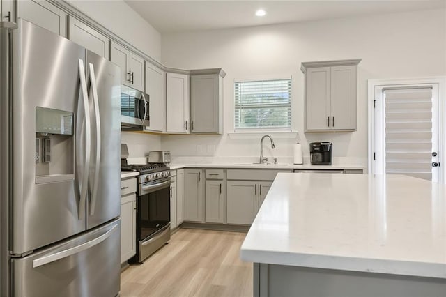 kitchen featuring light stone countertops, appliances with stainless steel finishes, gray cabinetry, sink, and light hardwood / wood-style floors