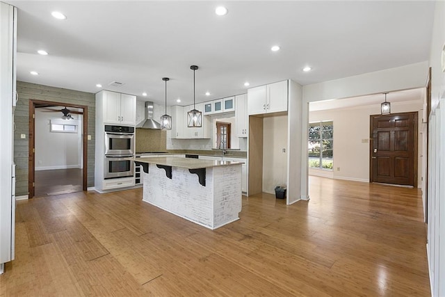 kitchen featuring a center island, wall chimney exhaust hood, tasteful backsplash, double oven, and white cabinets