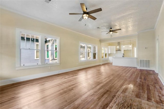 unfurnished living room featuring ceiling fan, crown molding, a wealth of natural light, and wood-type flooring