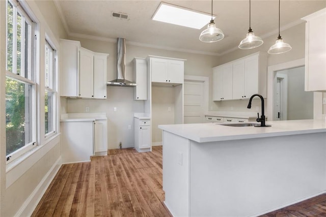 kitchen with wall chimney exhaust hood, sink, white cabinetry, light wood-type flooring, and pendant lighting