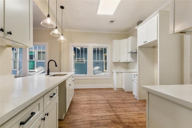 kitchen with sink, white cabinetry, light stone counters, ornamental molding, and pendant lighting