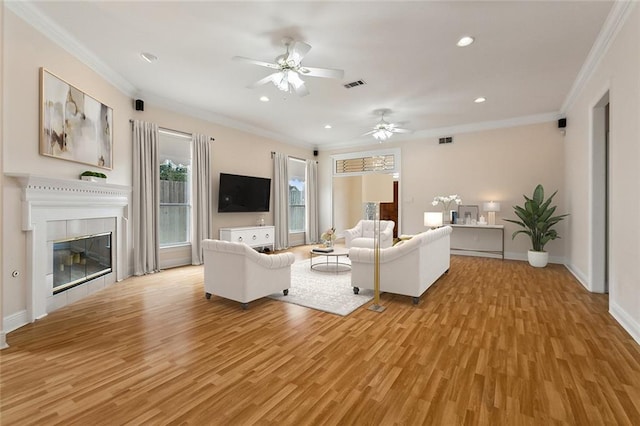 unfurnished living room featuring ceiling fan, ornamental molding, a baseboard heating unit, a tiled fireplace, and light wood-type flooring