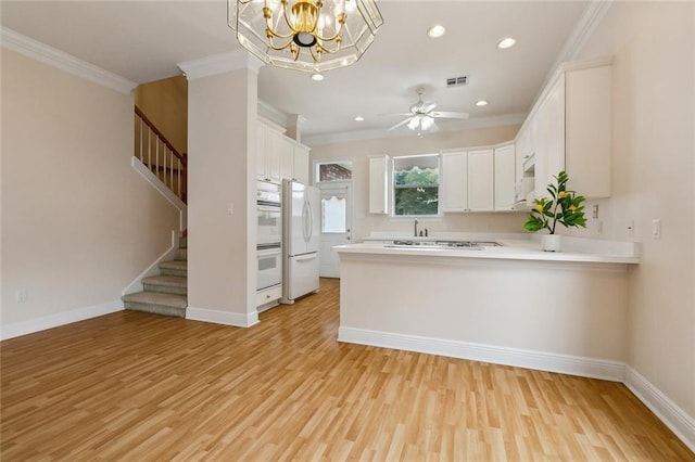 kitchen featuring white appliances, ceiling fan with notable chandelier, crown molding, kitchen peninsula, and white cabinetry