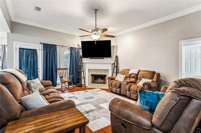 living room featuring ceiling fan, a fireplace, crown molding, and light hardwood / wood-style flooring