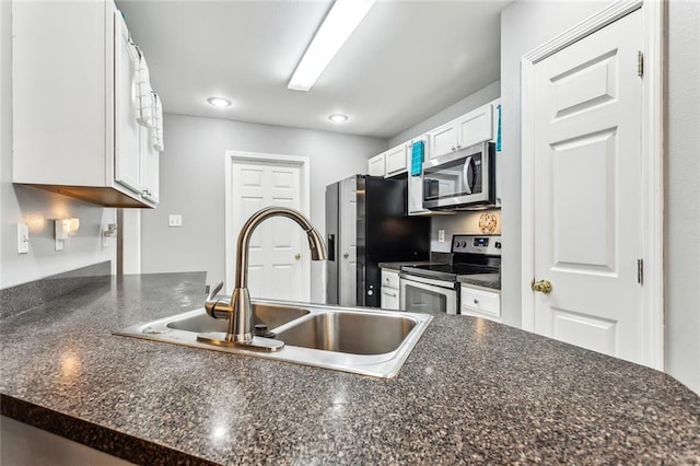 kitchen with appliances with stainless steel finishes, white cabinetry, dark stone countertops, and sink