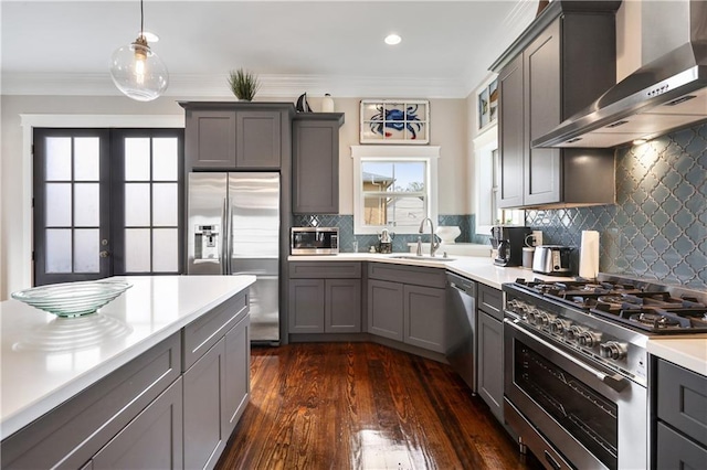 kitchen with sink, gray cabinetry, stainless steel appliances, decorative light fixtures, and wall chimney exhaust hood