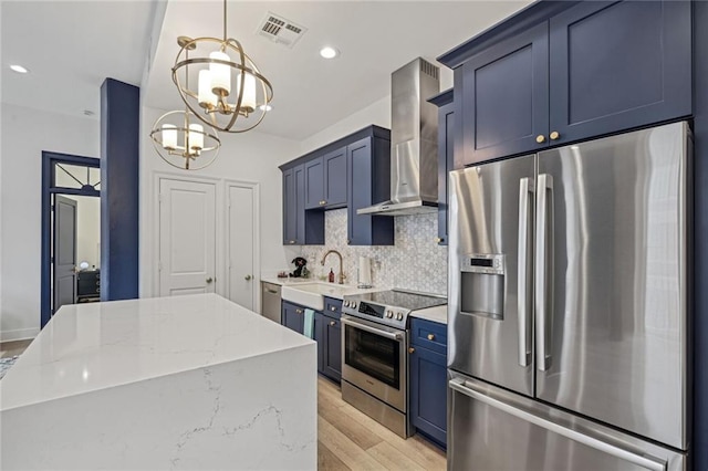 kitchen with stainless steel appliances, a notable chandelier, decorative light fixtures, wall chimney range hood, and light stone counters