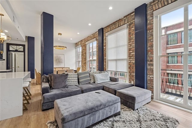 living room featuring light wood-type flooring, brick wall, and an inviting chandelier