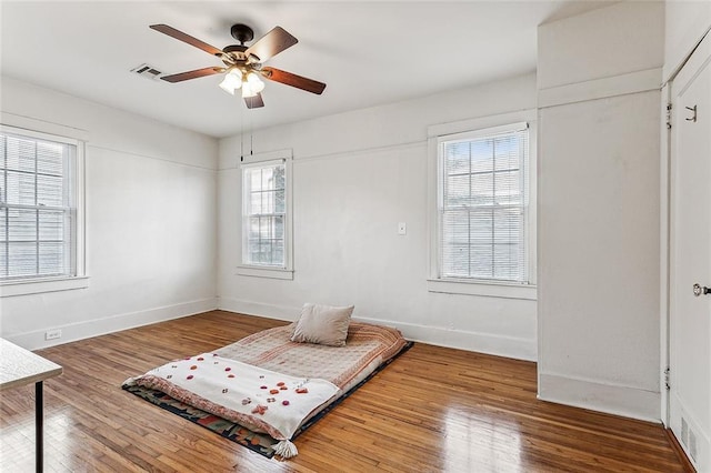 bedroom with multiple windows, wood-type flooring, and ceiling fan