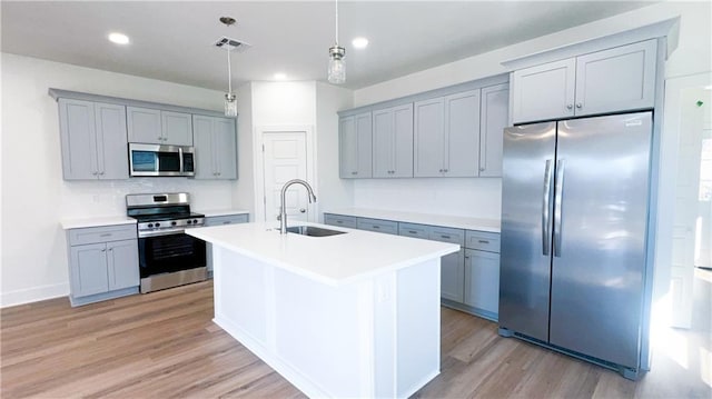 kitchen featuring sink, light hardwood / wood-style flooring, appliances with stainless steel finishes, a kitchen island with sink, and decorative light fixtures