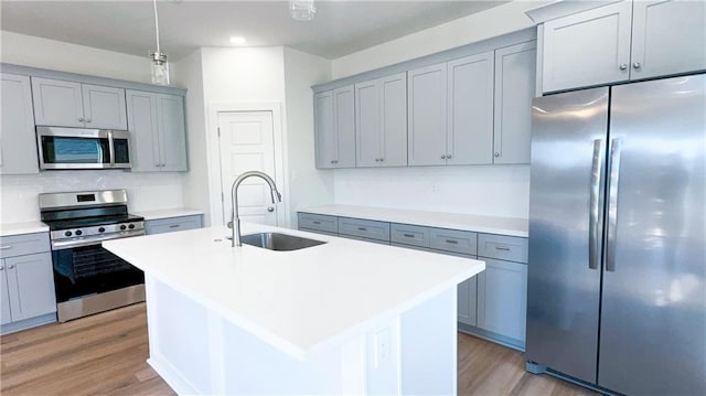 kitchen featuring sink, appliances with stainless steel finishes, light hardwood / wood-style floors, an island with sink, and decorative light fixtures