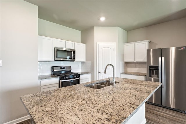 kitchen with light stone counters, stainless steel appliances, a kitchen island with sink, sink, and white cabinets