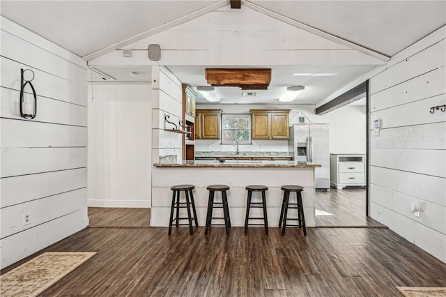 kitchen with kitchen peninsula, stainless steel fridge, dark hardwood / wood-style flooring, and wood walls