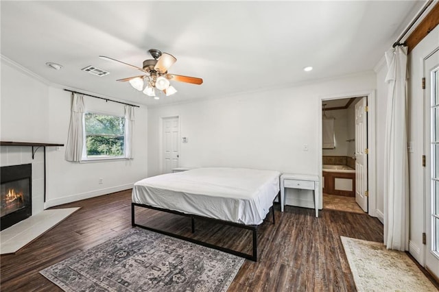 bedroom with ceiling fan, dark hardwood / wood-style flooring, a tile fireplace, and ensuite bath