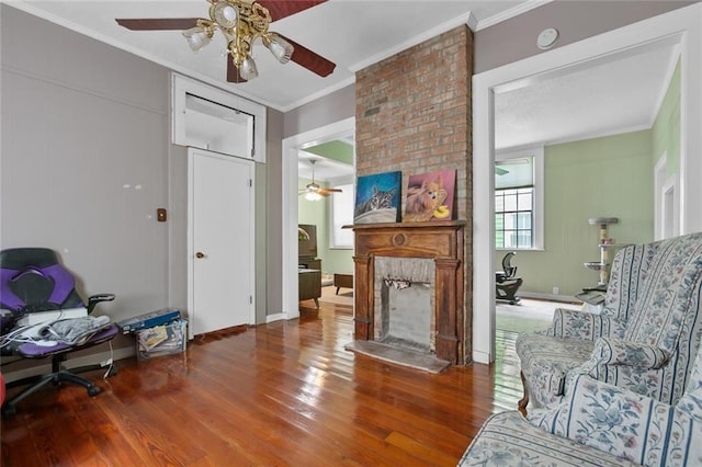 sitting room with hardwood / wood-style flooring, ceiling fan, crown molding, and a brick fireplace