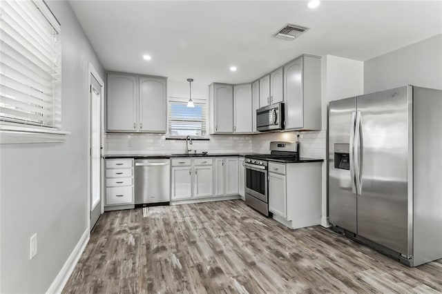 kitchen featuring appliances with stainless steel finishes, backsplash, sink, decorative light fixtures, and light hardwood / wood-style floors