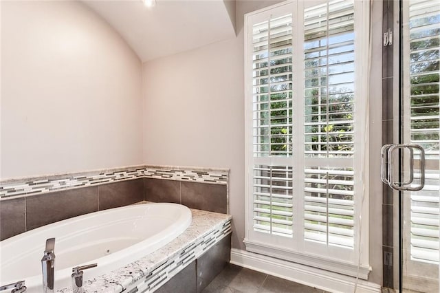 bathroom with tile patterned flooring, a relaxing tiled tub, and vaulted ceiling