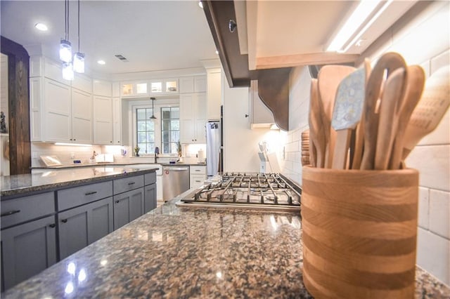 kitchen featuring stainless steel appliances, dark stone counters, decorative light fixtures, gray cabinets, and white cabinets