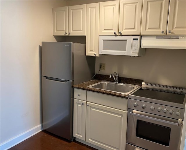 kitchen with white cabinets, dark countertops, appliances with stainless steel finishes, under cabinet range hood, and a sink