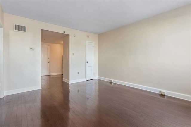 spare room with dark wood-style flooring, visible vents, and baseboards