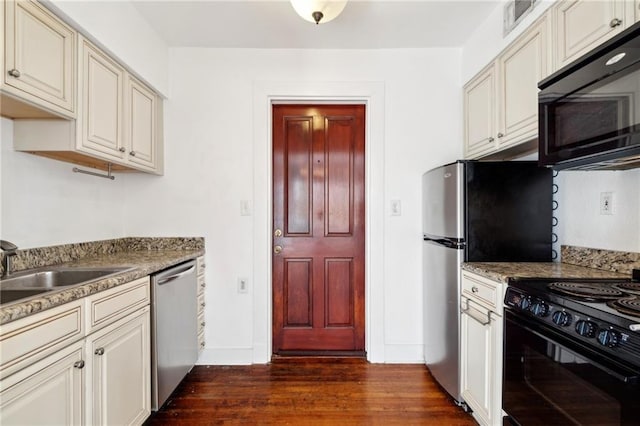 kitchen featuring stone counters, black appliances, sink, dark hardwood / wood-style floors, and cream cabinetry