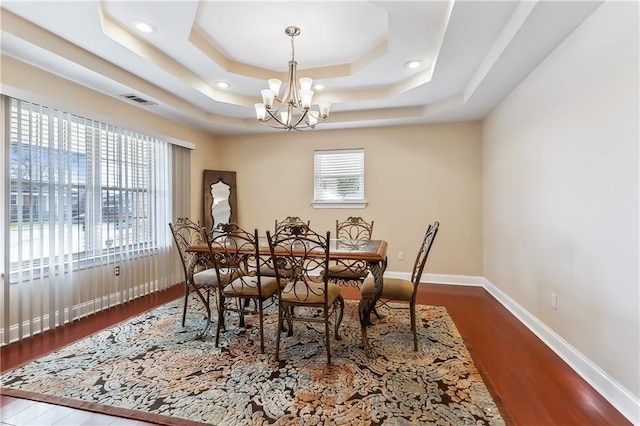 dining area with dark hardwood / wood-style floors, a raised ceiling, and a chandelier