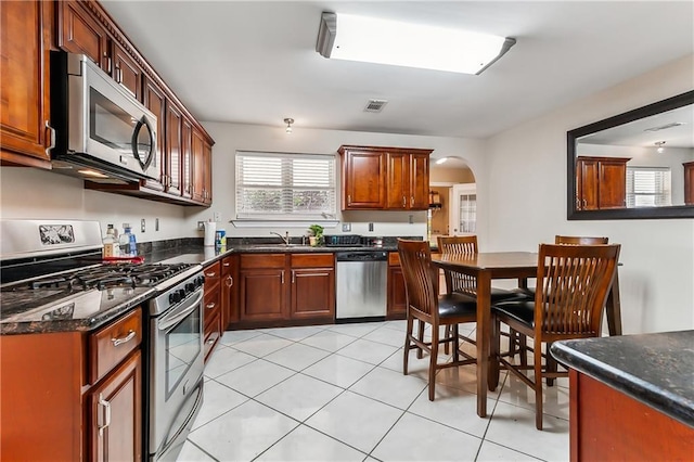 kitchen featuring dark stone countertops, sink, light tile patterned floors, and stainless steel appliances