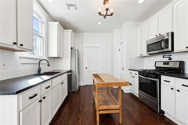 kitchen with appliances with stainless steel finishes, sink, a chandelier, white cabinets, and dark hardwood / wood-style floors