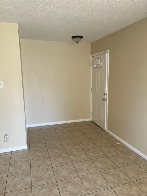 empty room with a textured ceiling, light tile patterned floors, and baseboards