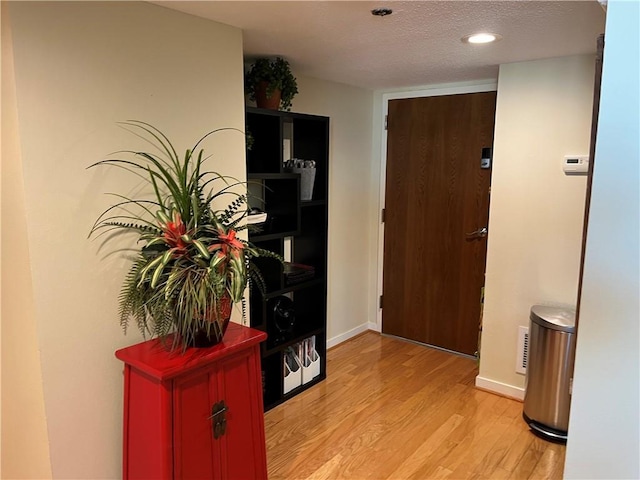 hallway with light wood-type flooring and a textured ceiling