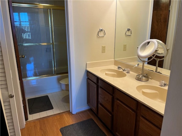 full bathroom featuring shower / bath combination with glass door, hardwood / wood-style floors, vanity, and toilet