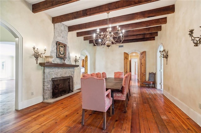 dining area with beam ceiling, a stone fireplace, wood-type flooring, and an inviting chandelier