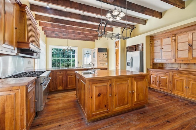 kitchen featuring stainless steel appliances, sink, beam ceiling, decorative light fixtures, and an island with sink